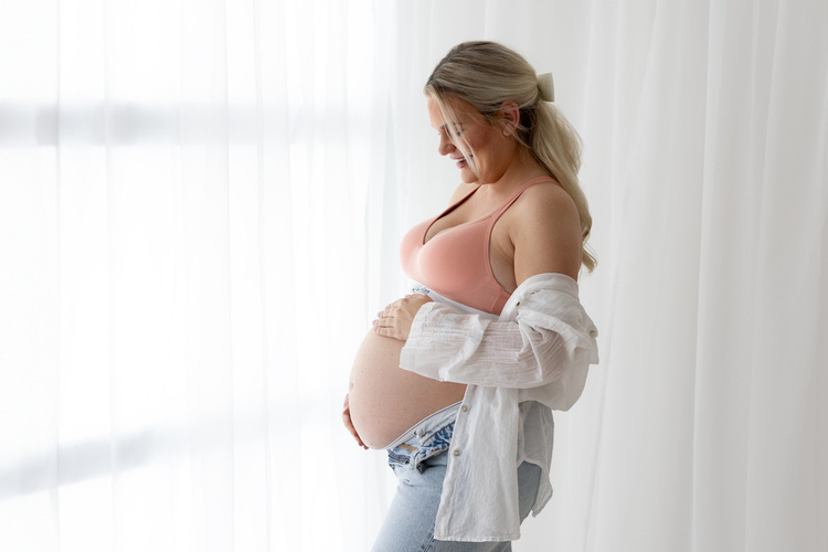 Denim used in maternity photoshoot with Jeans, with mum standing at a window, looking at, and holding her bump