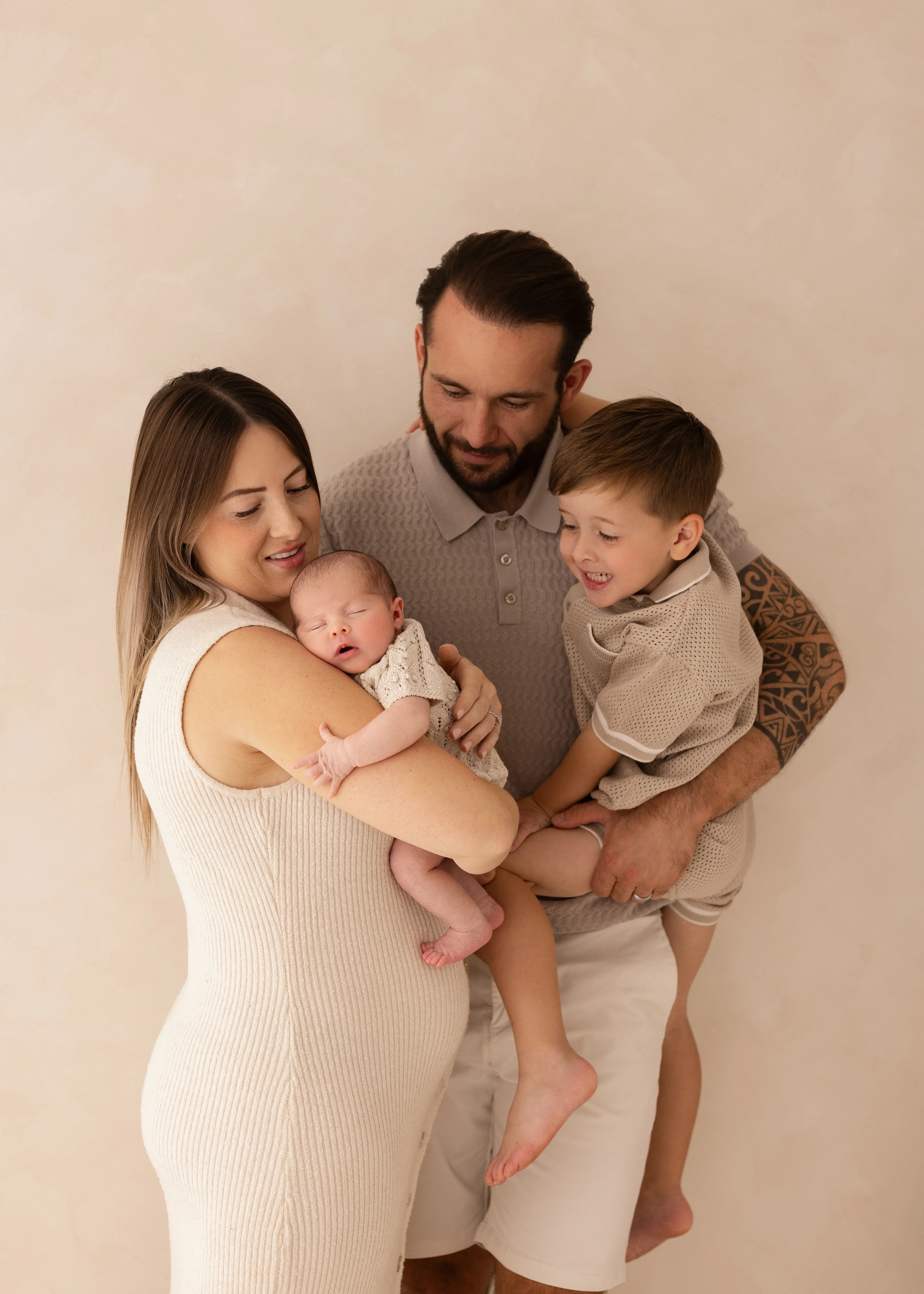 Parents holding their newborn baby while the older sibling smiles beside them, captured in a soft, natural family newborn photoshoot in Kent.