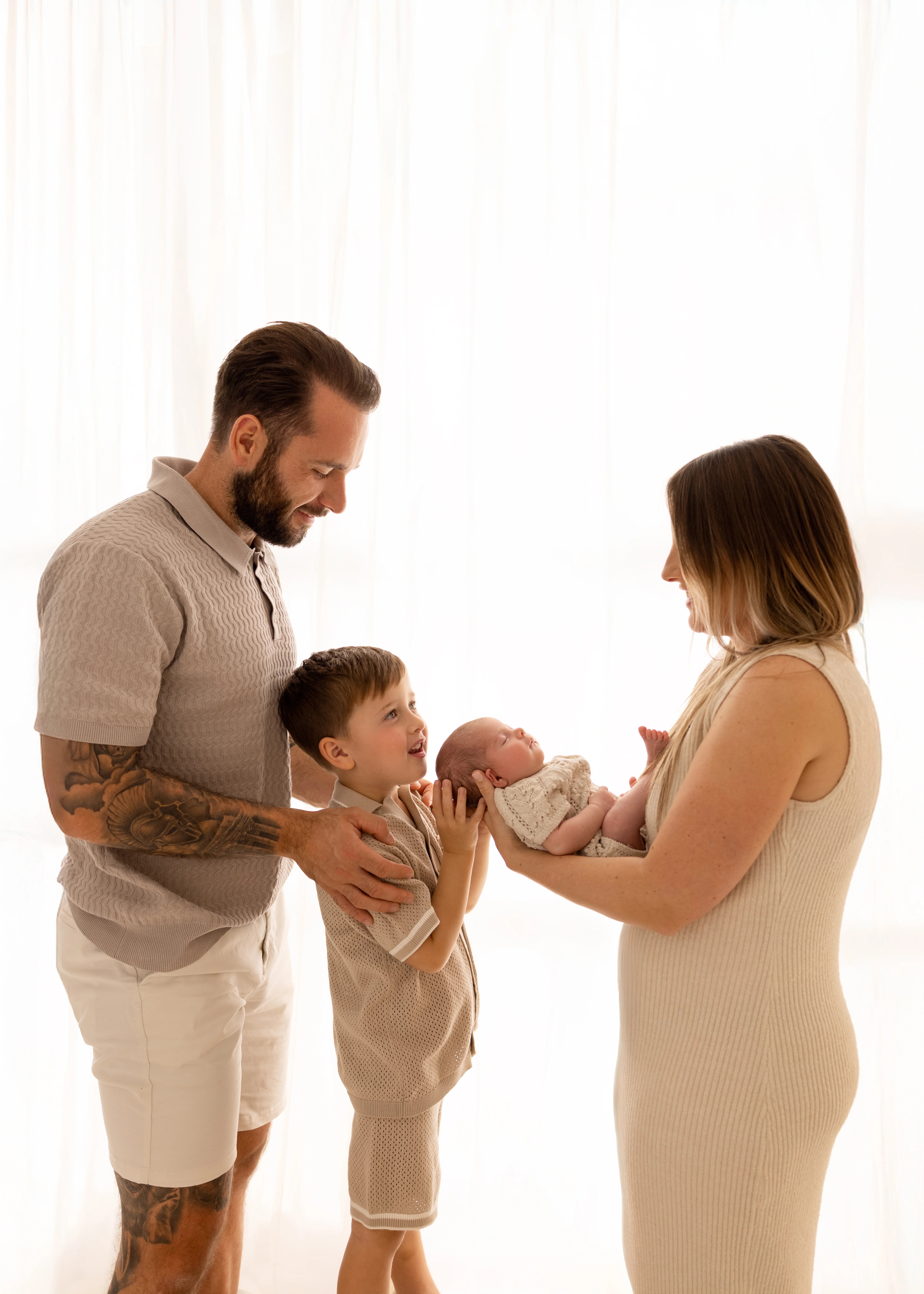 Parents and older brother gathered around their newborn baby, smiling and holding the baby together during a soft, natural family newborn photoshoot in Kent.