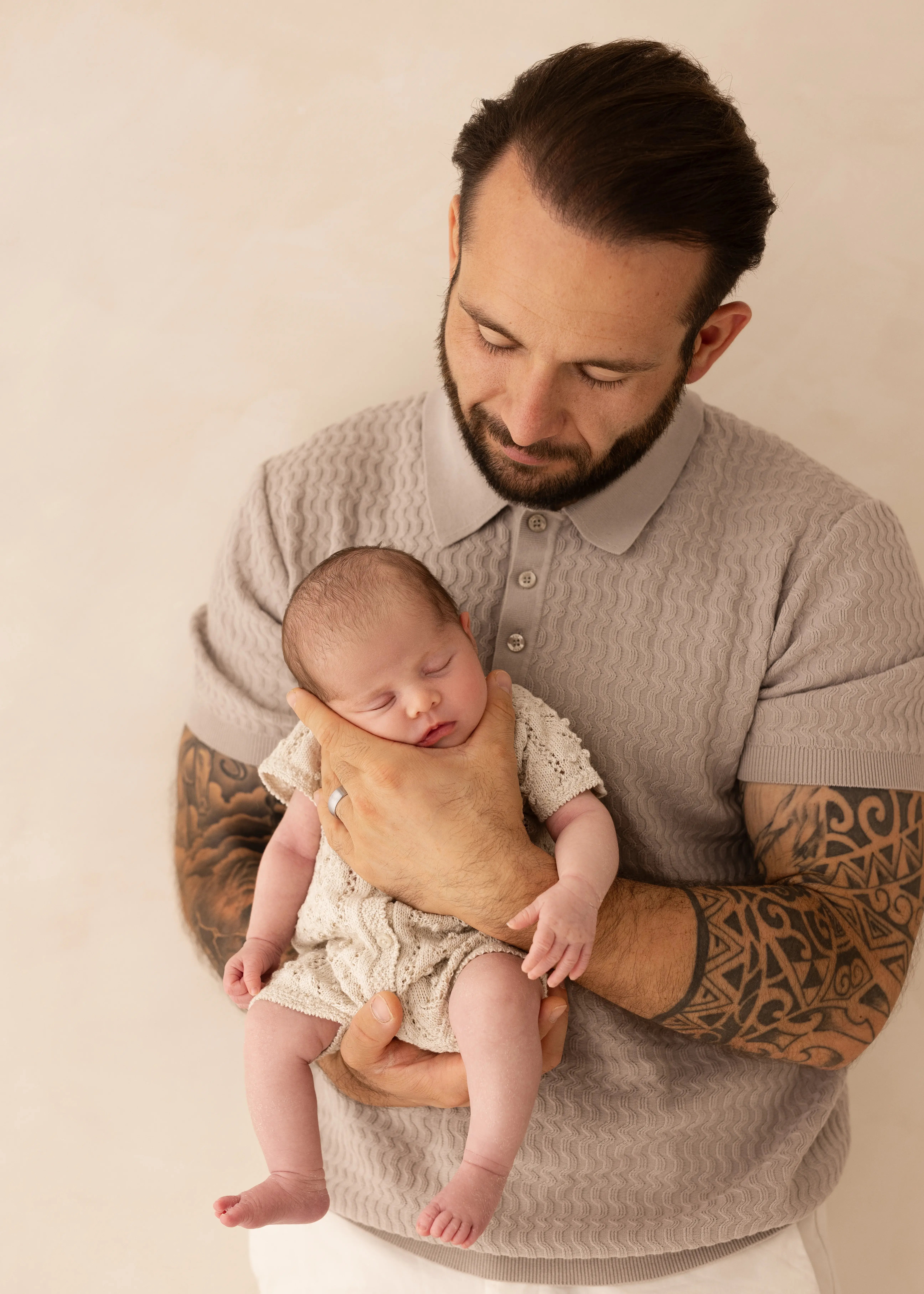Father gently cradling his sleeping newborn baby dressed in a cream knitted outfit during a soft, natural newborn photoshoot in Kent.
