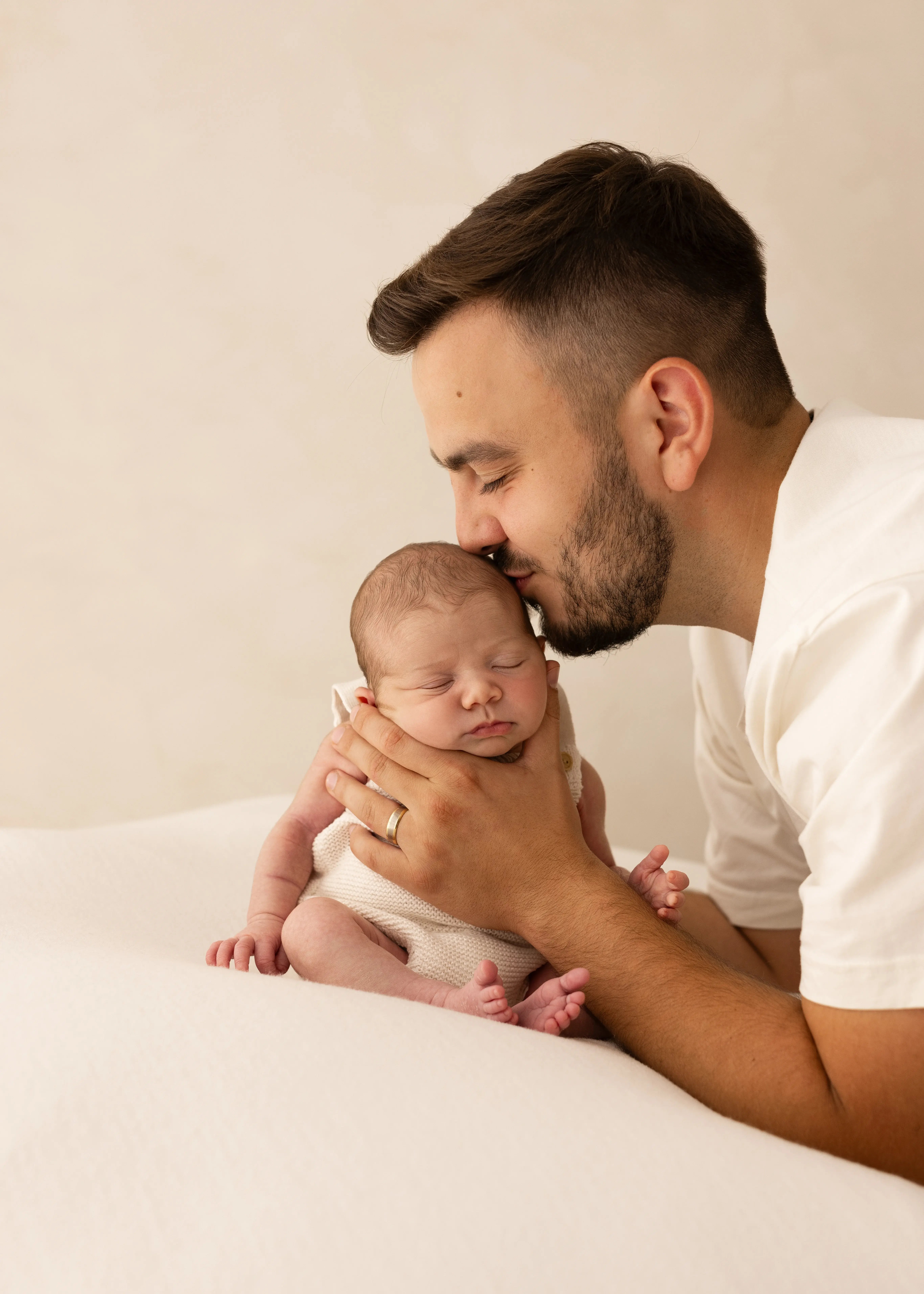 Father holding his sleeping newborn baby and gently kissing their head during a soft, natural newborn photoshoot in Kent.