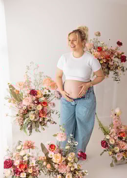 Photograph from a maternity shoot, showing a pregnant female in blue jeans and a white top holding her bump