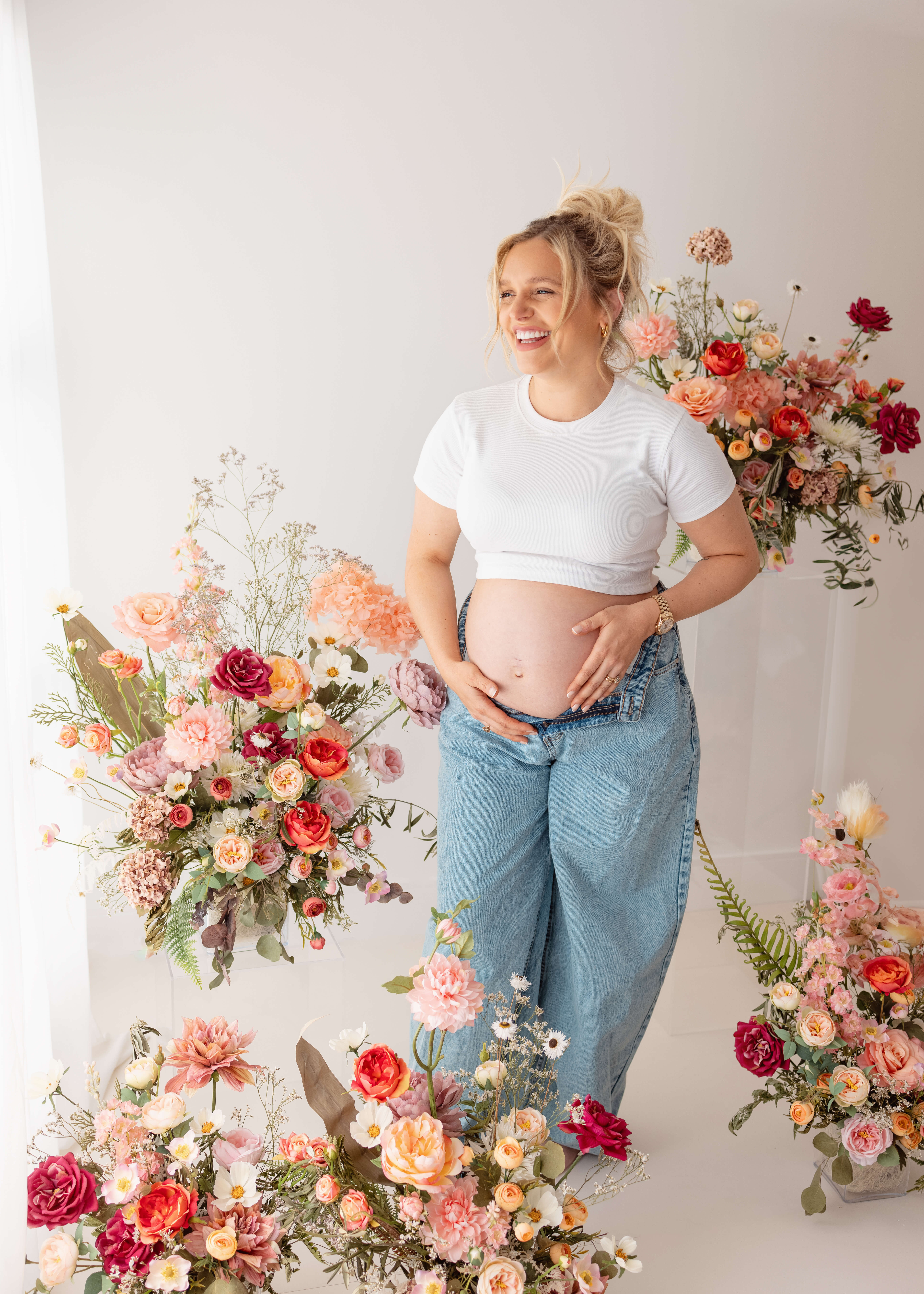 Photograph from a maternity shoot, showing a pregnant female in blue jeans and a white top holding her bump