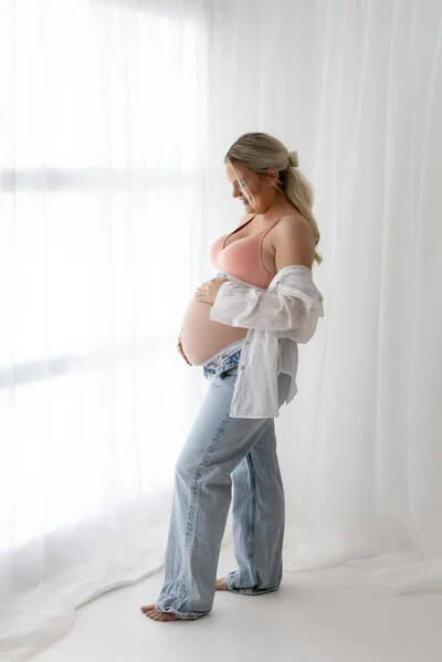 Denim used in maternity photoshoot with Jeans, with mum standing at a window, looking at, and holding her bump