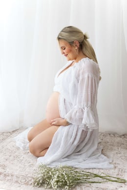 White dress for maternity photoshoot used, with mum kneeling and looking at her bump