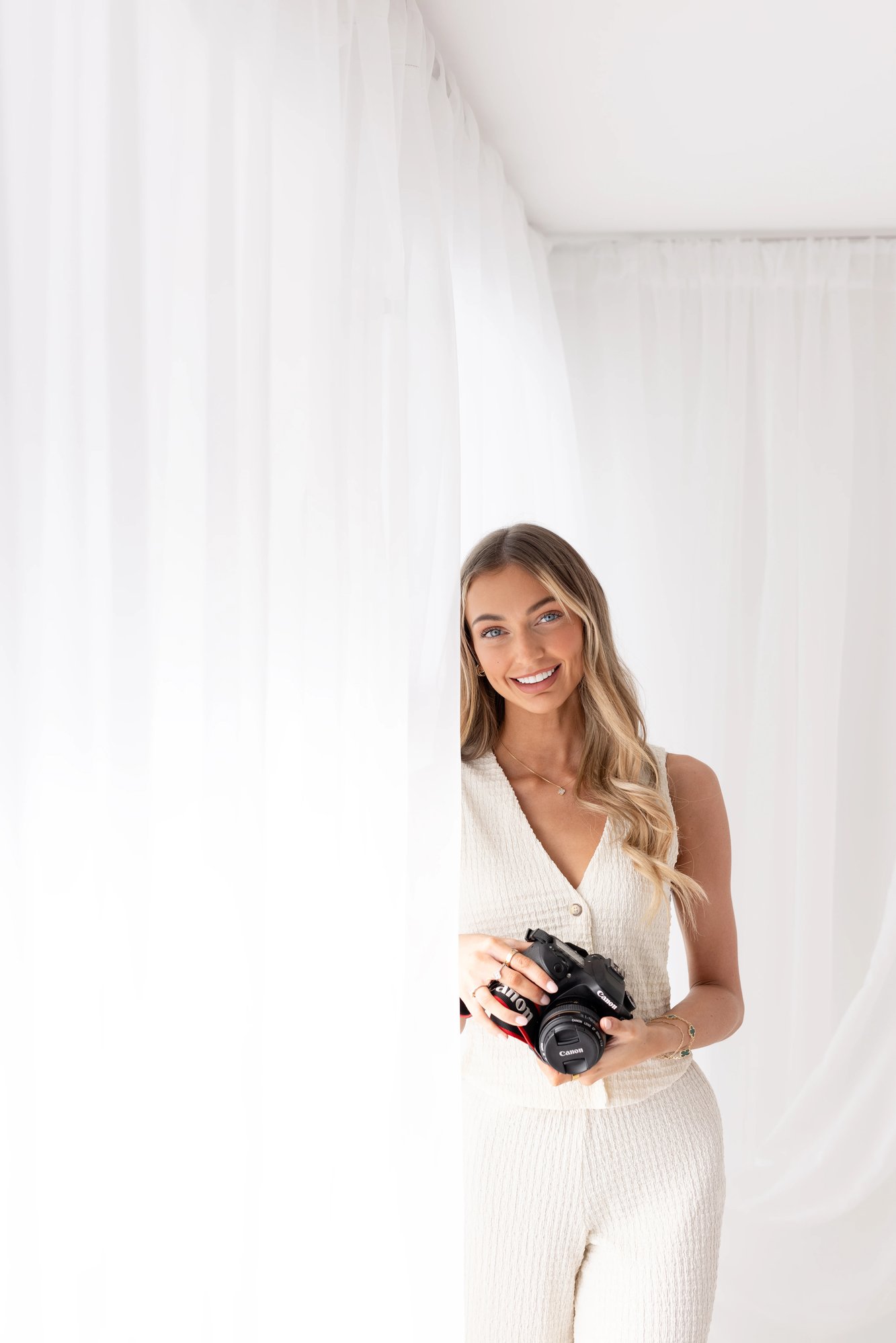 Molly Ann, the owner of Before Time Flies Photography, smiling while holding her camera in the light and airy studio.