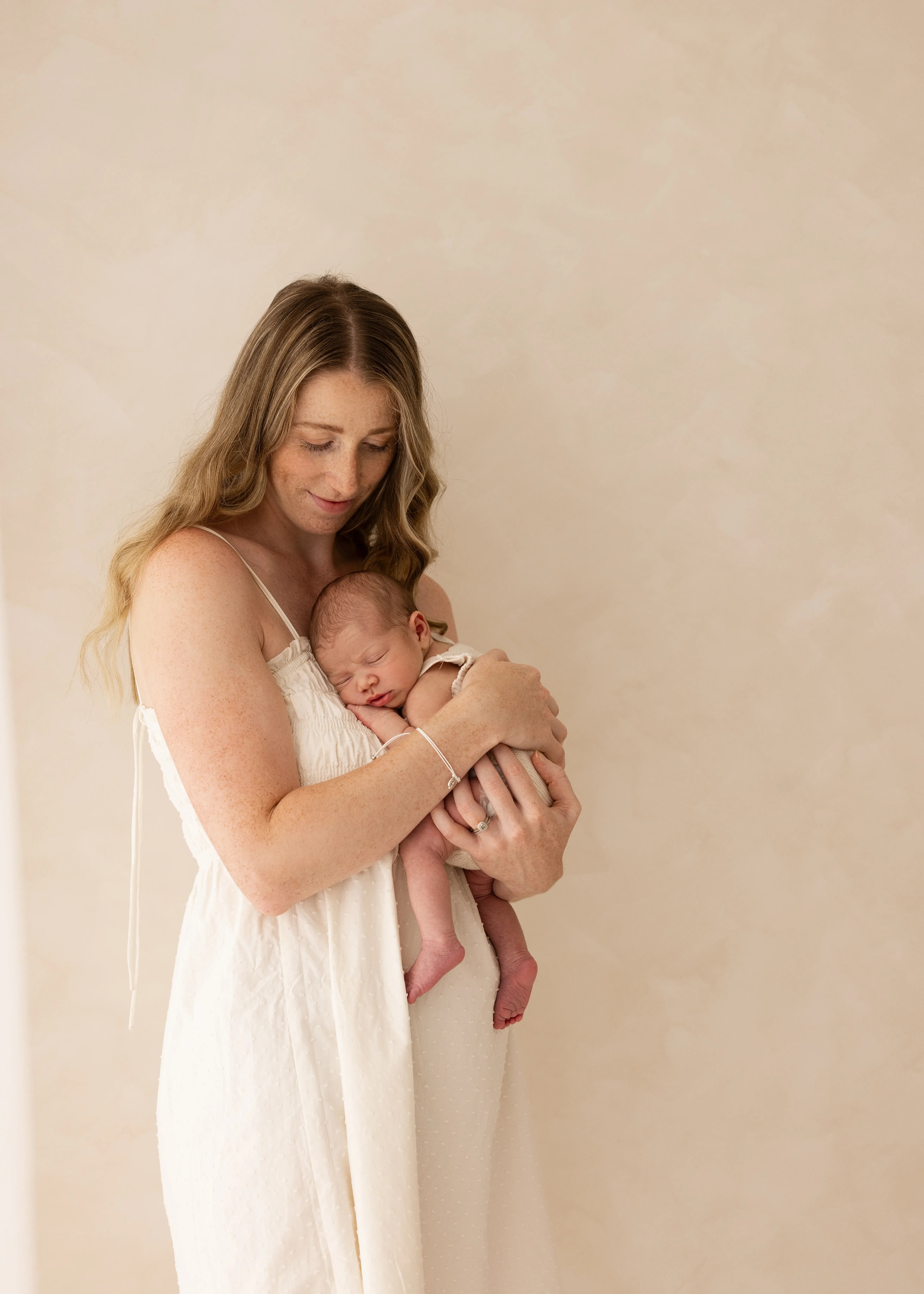 Mother gently holding her sleeping newborn baby against her chest during a soft, natural newborn photoshoot in Kent.