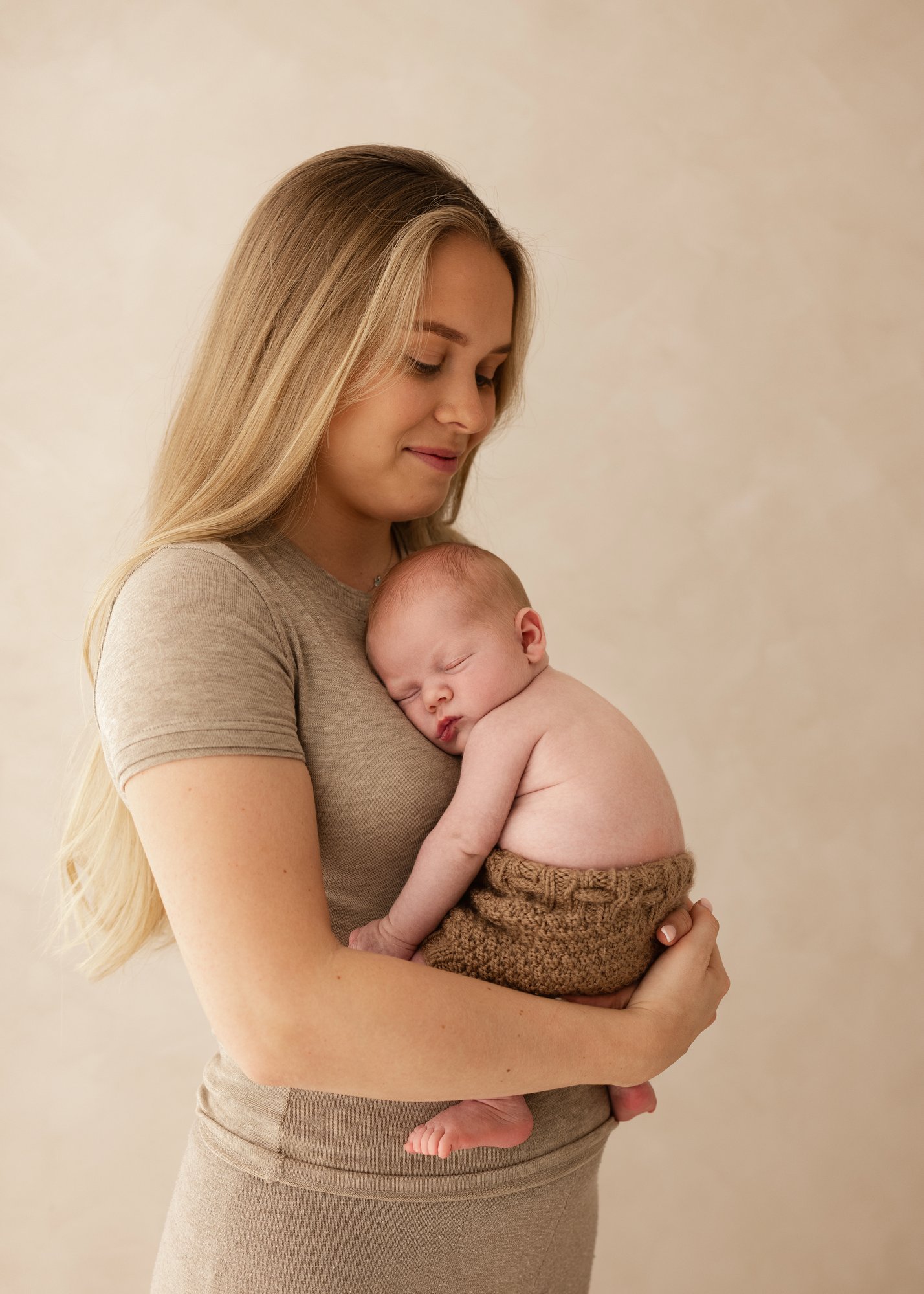 Mother holding her sleeping newborn baby against her chest, photographed in warm neutral tones at the Before Time Flies studio.
