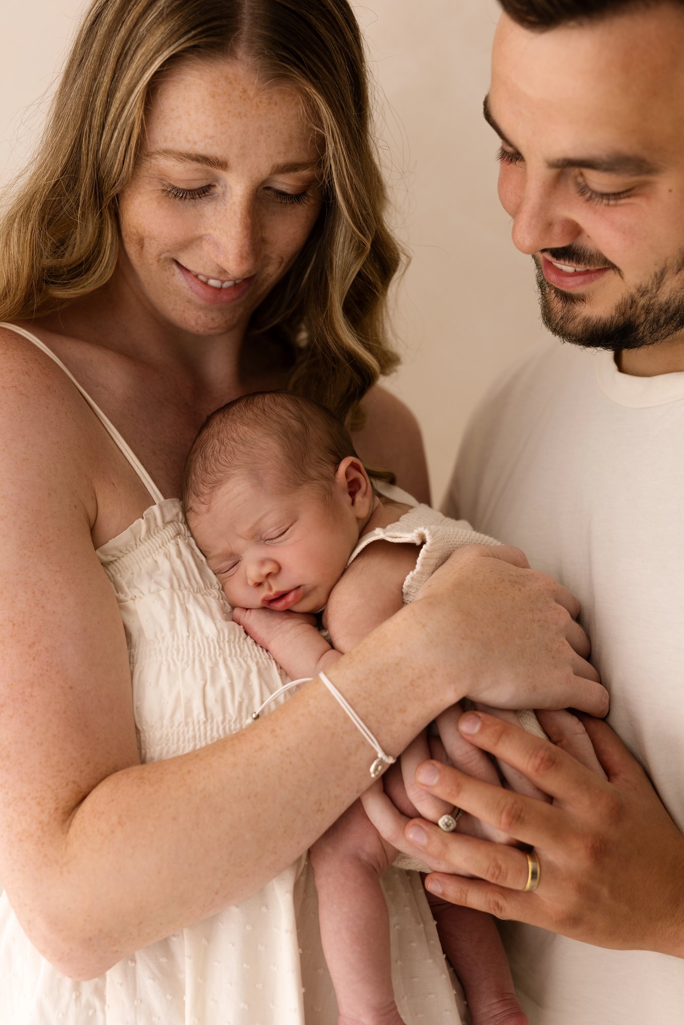 Close-up portrait of two parents gently holding their sleeping newborn, captured in soft neutral tones during a natural newborn photography session.