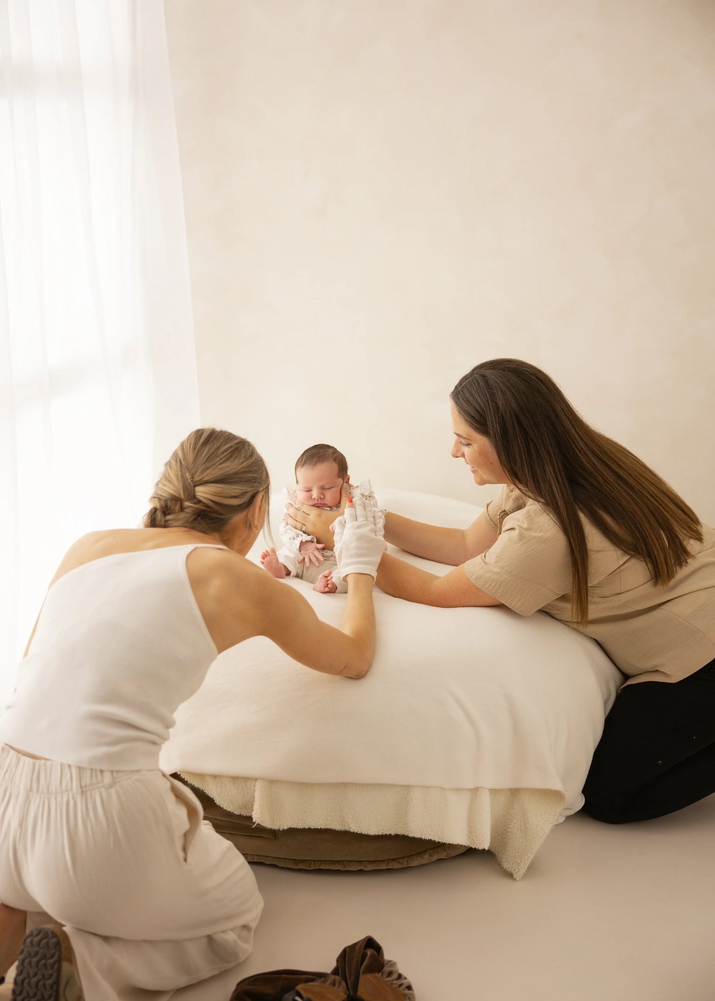 Two women carefully posing a newborn baby on a padded beanbag during a studio photoshoot, showing safe newborn handling behind the scenes.