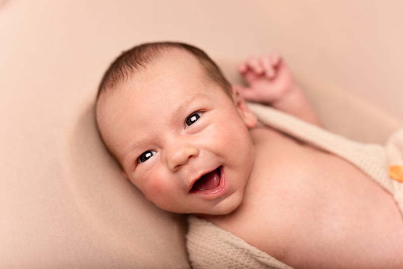 newborn baby photo of them smiling and awake, looking towards the camera at their mum