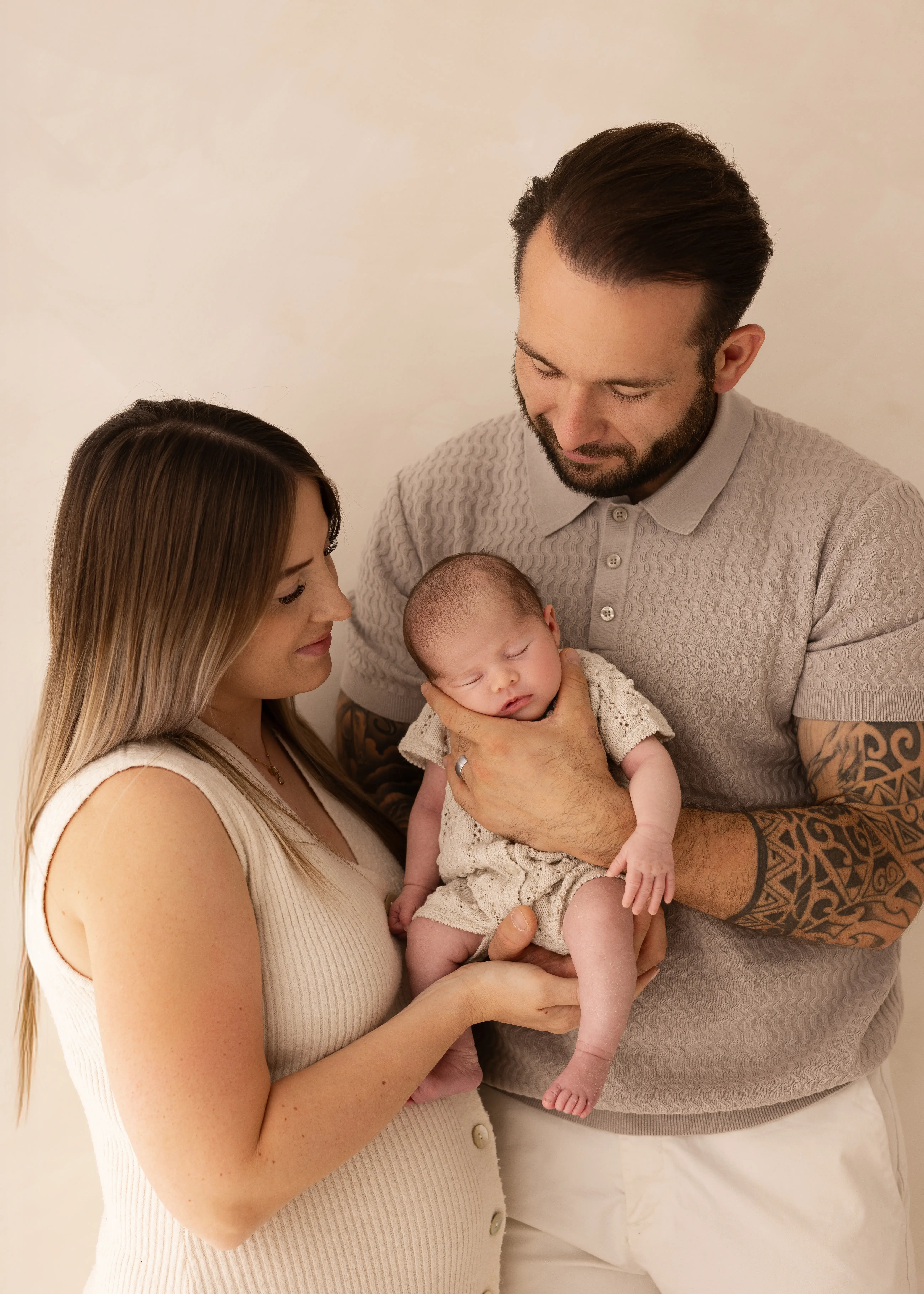 Mother and father holding their sleeping newborn baby together, looking down lovingly during a soft, natural family newborn photoshoot in Kent.