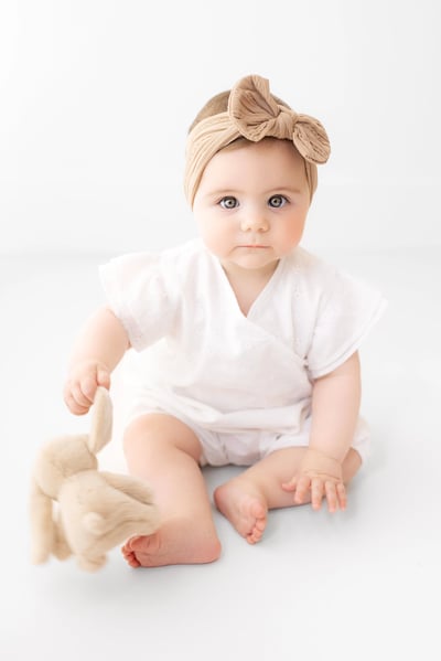 Baby photographed with a cuddly rabbit toy, wearing a bow on their head