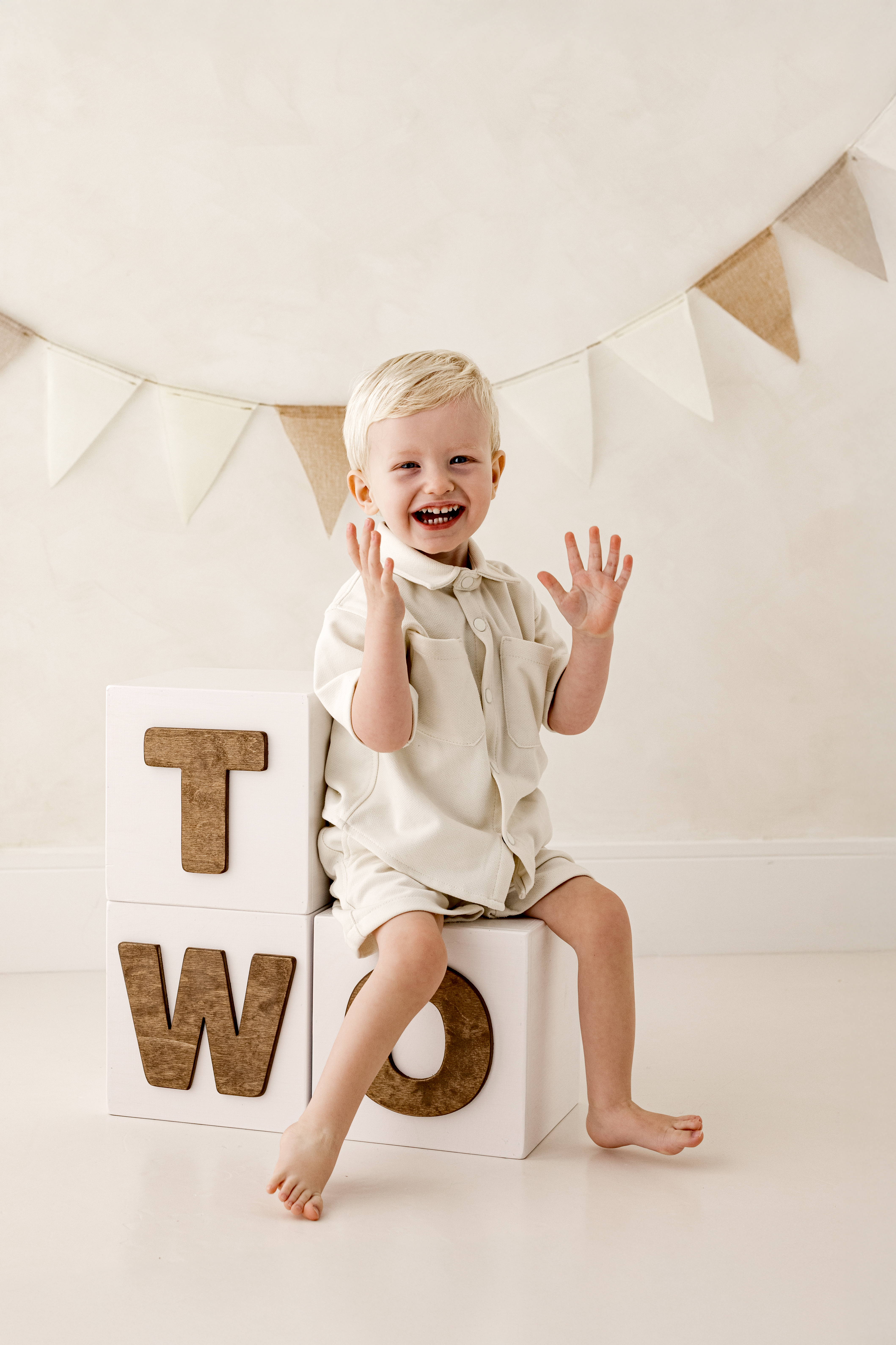 Smiling toddler sitting on white photo blocks spelling "TWO", celebrating their second birthday in a natural-toned milestone photography session in Kent.